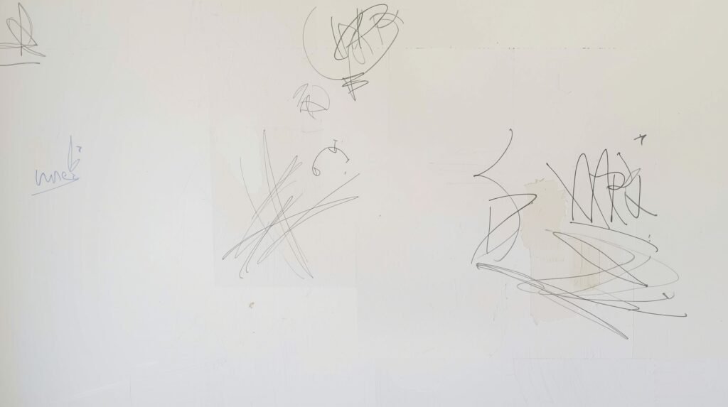 Dry erase marker scribbles and stains visible on a painted wall before cleaning.